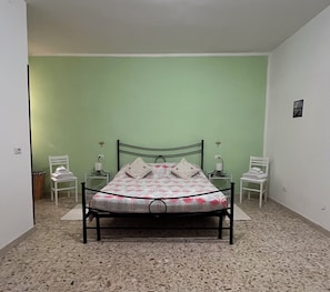 Un dormitorio con una cama, dos mesitas de noche, una silla y un cuadro colgado en la pared.