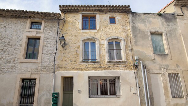 A two-story building with a stone facade, multiple windows with metal bars, and a small door.