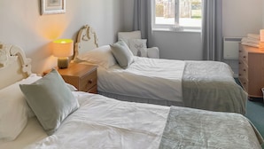 A hotel room with two beds, a bedside table with a lamp, a dresser, and a window with curtains.