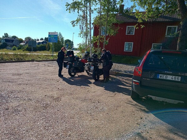 Un estacionamiento de grava con dos motocicletas y un automóvil.