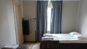 Una habitación con dos camas, piso de madera, ventana con cortinas e iluminación colgante.