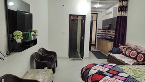 Habitación de hotel con cama, escritorio, silla, televisor y una kitchenette pequeña.