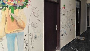 Un pasillo con un mural de una persona sosteniendo un ramo, una puerta cerrada y una pared con varios dibujos y notas.