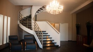 Un intérieur moderne avec un escalier en colimaçon, un lustre et deux fauteuils en cuir noir.