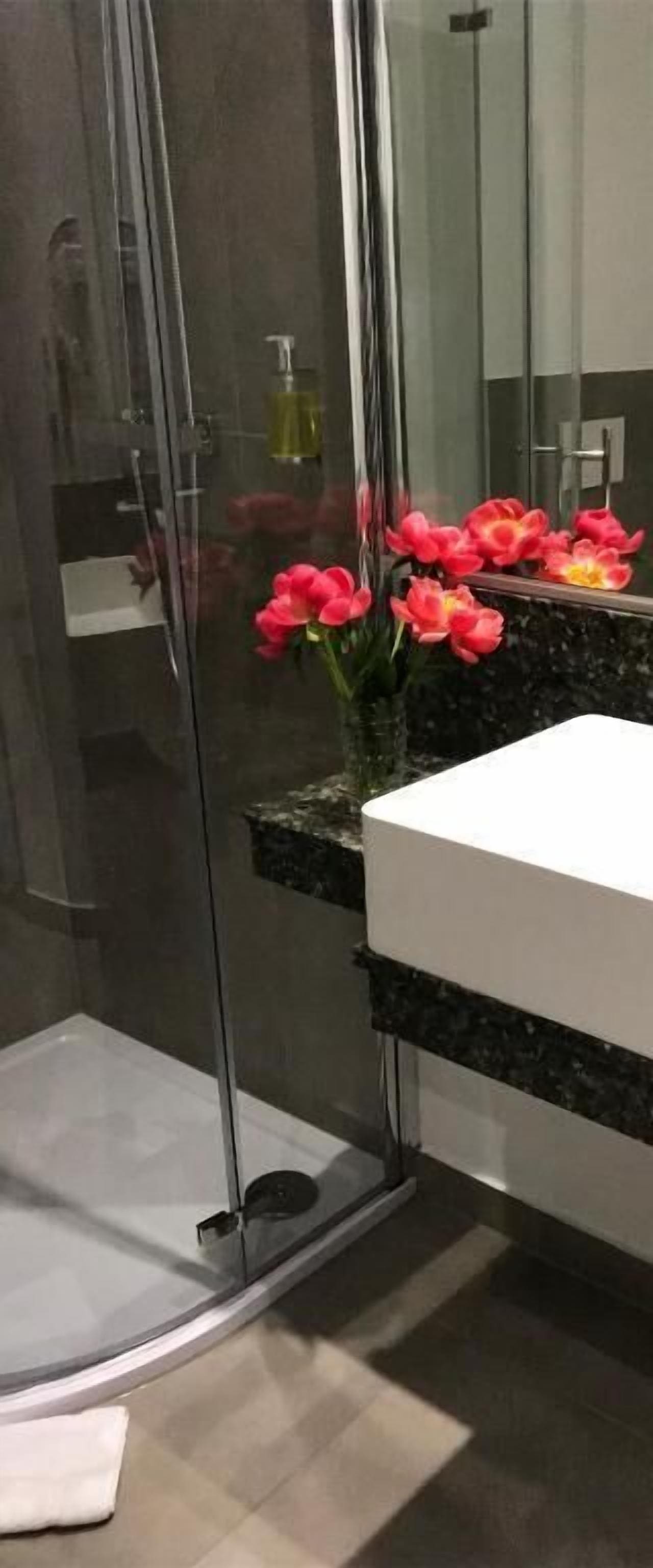 A modern bathroom with a glass-enclosed shower, a white sink, and a marble countertop.