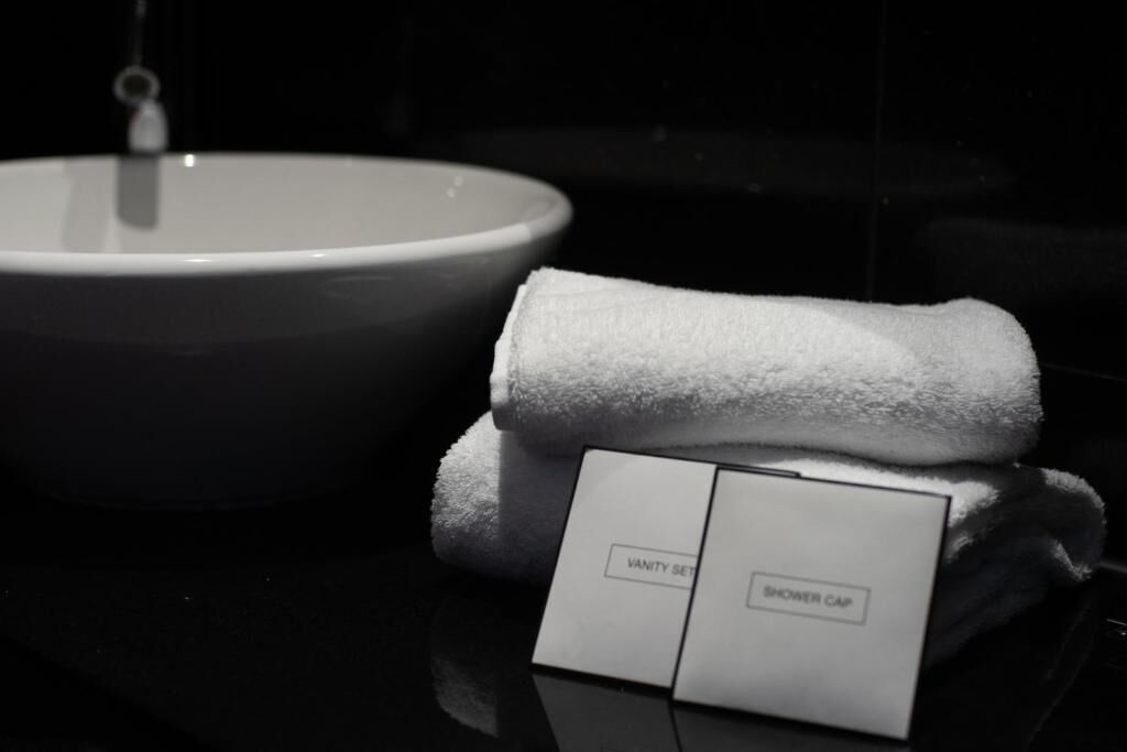 Un lavabo de salle de bain et une serviette pliée, accompagnés d’une pancarte indiquant la présence d’un nécessaire de toilette et d’un bonnet de douche.