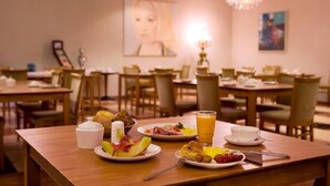 Une table de petit-déjeuner avec plusieurs tables, chacune étant dressée avec des assiettes de nourriture, des tasses et un verre de jus d’orange.