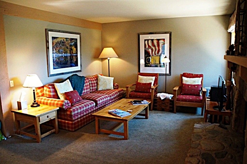 A cozy living room with a sofa, two armchairs, a coffee table, and a lamp. There are framed pictures on the wall.
