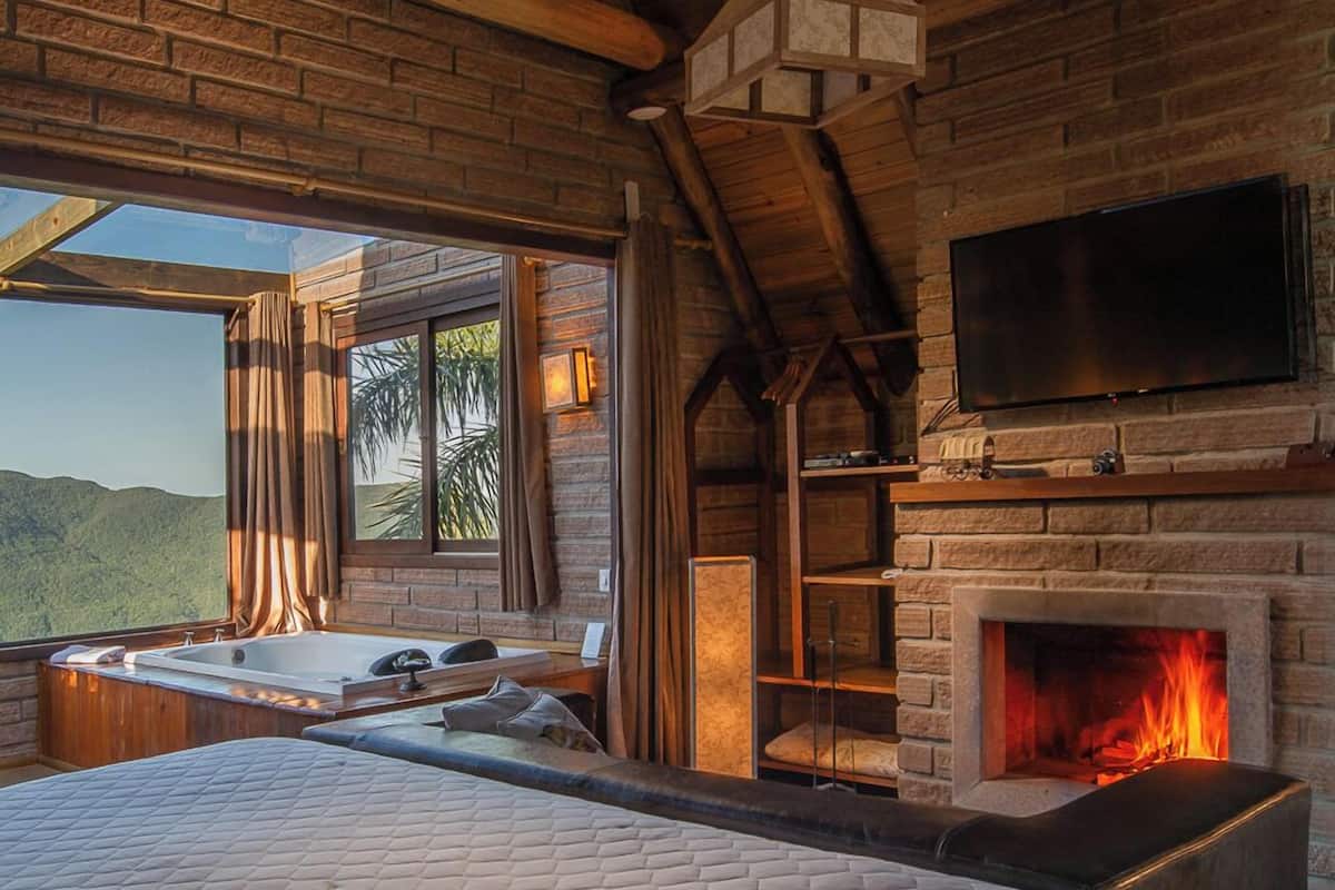 Ein Schlafzimmer mit einem großen Bett, einem Kamin, einem Fernseher und Blick ins Freie.