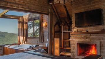 Un dormitorio con una cama grande, chimenea, televisor y vistas al exterior.
