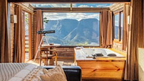 A room with a large window, a wooden bathtub, a telescope, and a cozy bed. - Morada dos Canyons (Praia Grande)