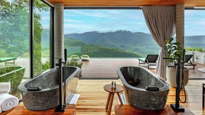 A modern spa area with two stone tubs, wooden flooring, and a view of mountains. - Morada dos Canyons (Praia Grande)