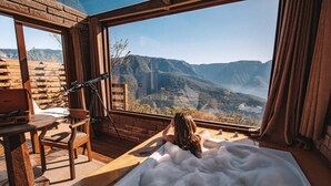 A room with a large window overlooking a mountainous landscape, a wooden desk with a laptop, and a bathtub filled with bubbles. - Morada dos Canyons (Praia Grande)