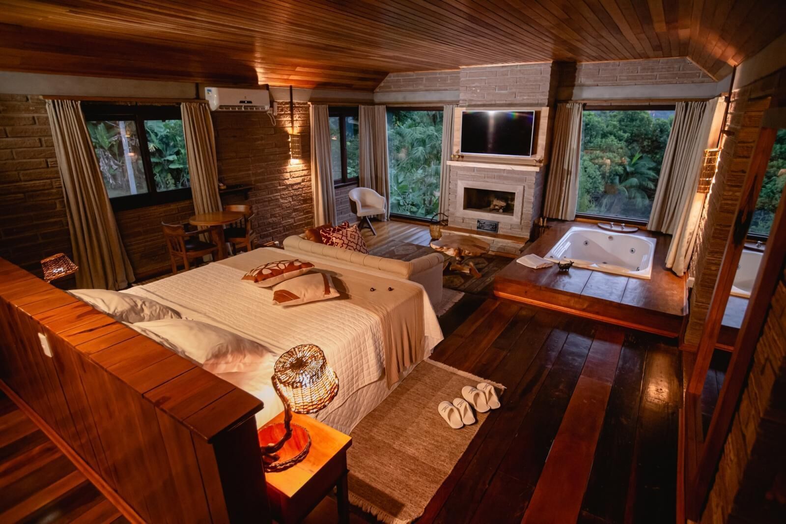 A spacious bedroom with a large bed, a sitting area with a fireplace, and a view of the outdoors.