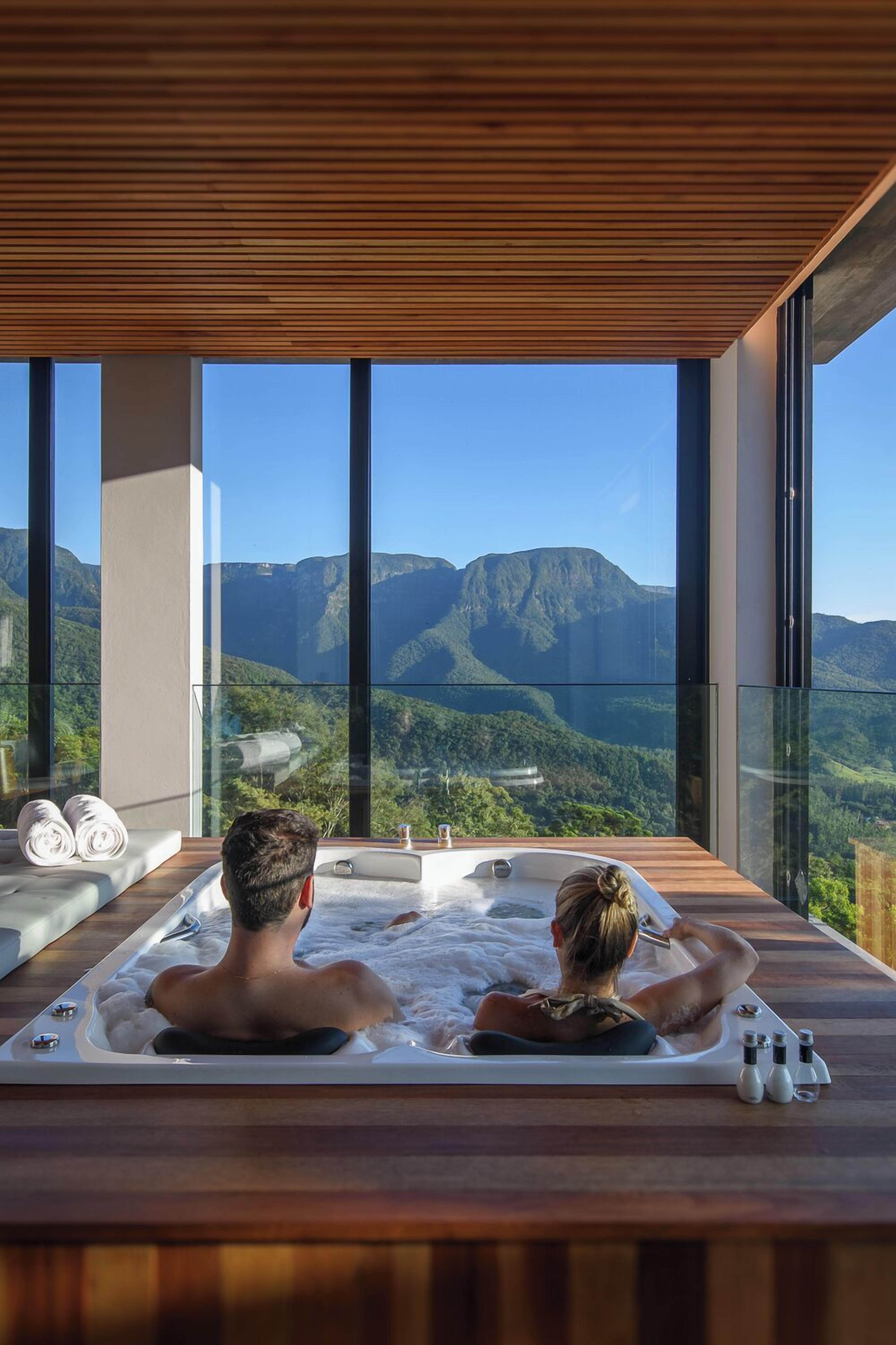 Um casal relaxando em uma banheira de hidromassagem com vista para as montanhas.