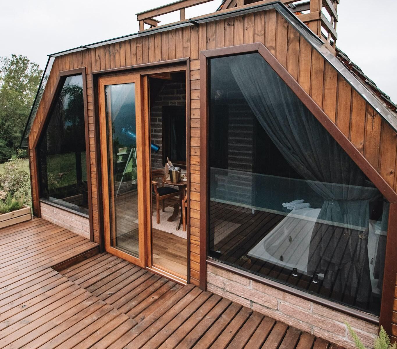 A modern wooden cabin with large glass windows and a deck.