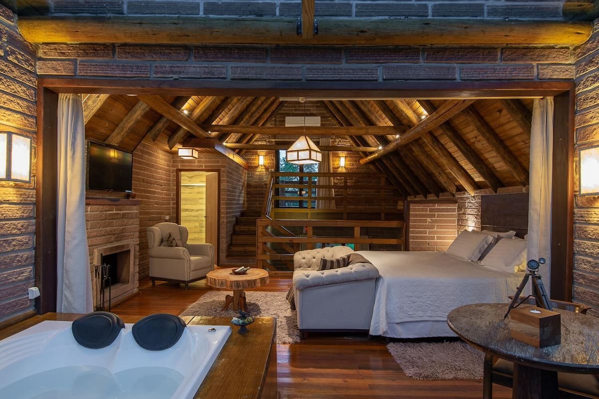 Ein gemütliches Schlafzimmer in einer Blockhütte mit Kamin, einer Couch, einem Bett und einer Whirlwanne.