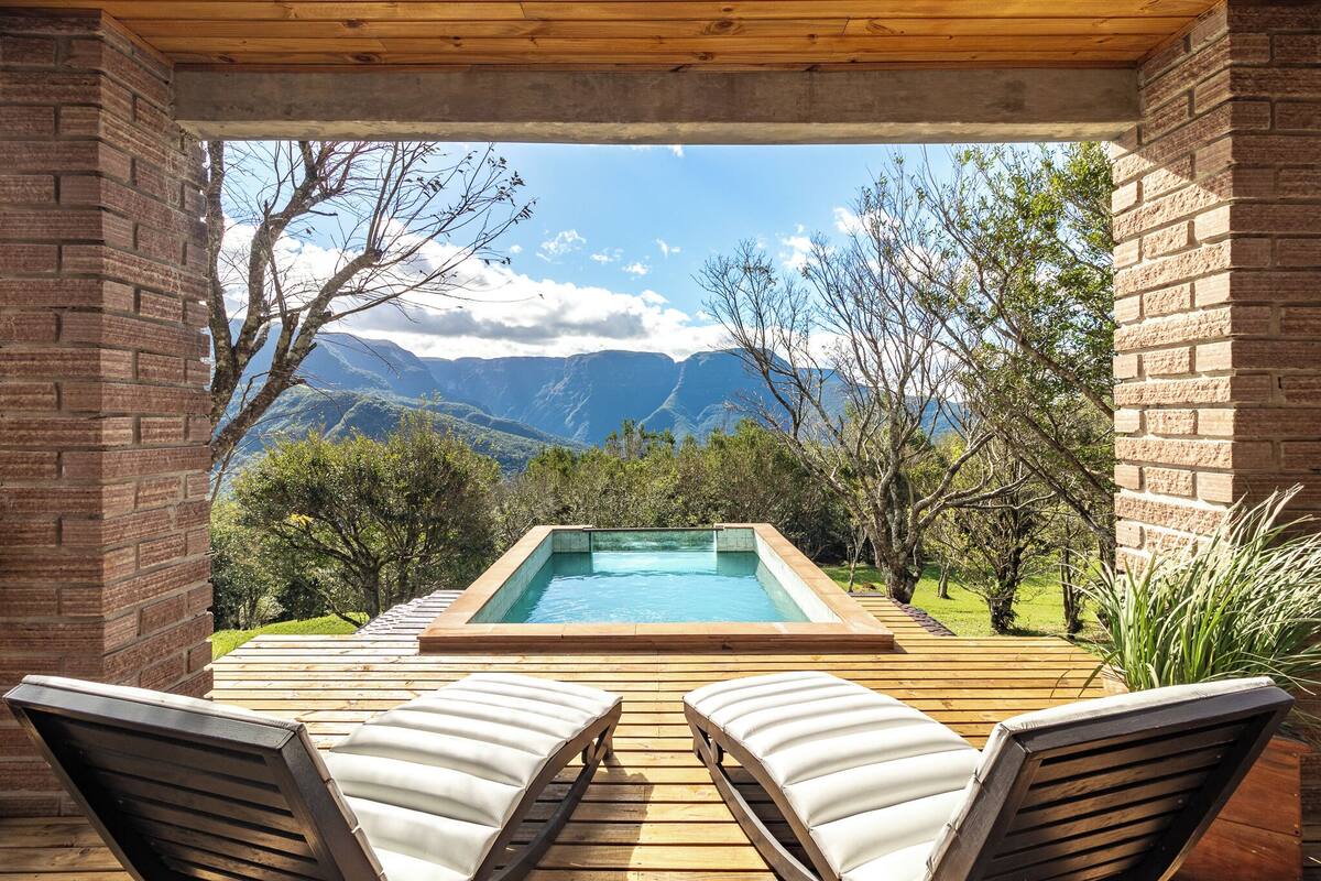Ein Whirlpool mit Holzterrasse und zwei Liegestühlen, mit Blick auf eine Berglandschaft.