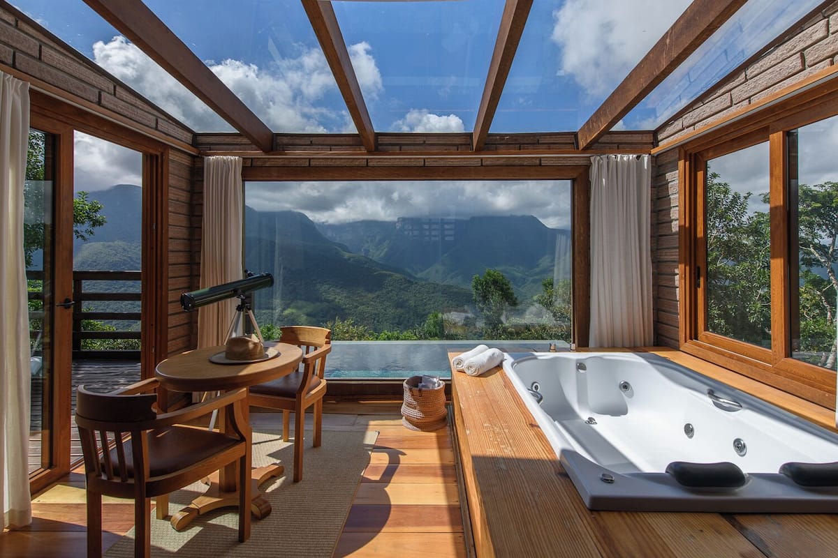 Ein Zimmer mit Holzeinrichtung, einem großen Fenster, einem Tisch mit Stühlen und einer Whirlwanne.