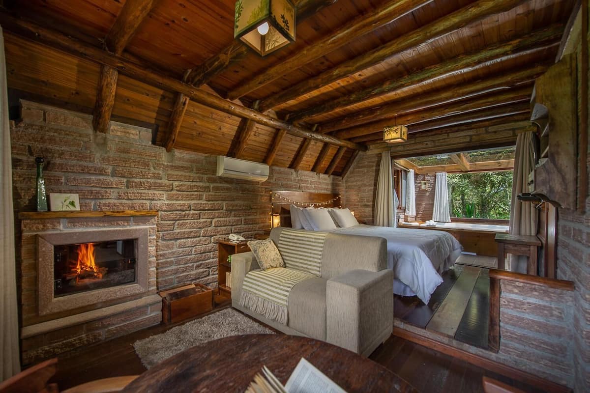 Ein gemütliches Blockhaus-Interieur mit Kamin, einem Bett, einer Couch und einem Esstisch.