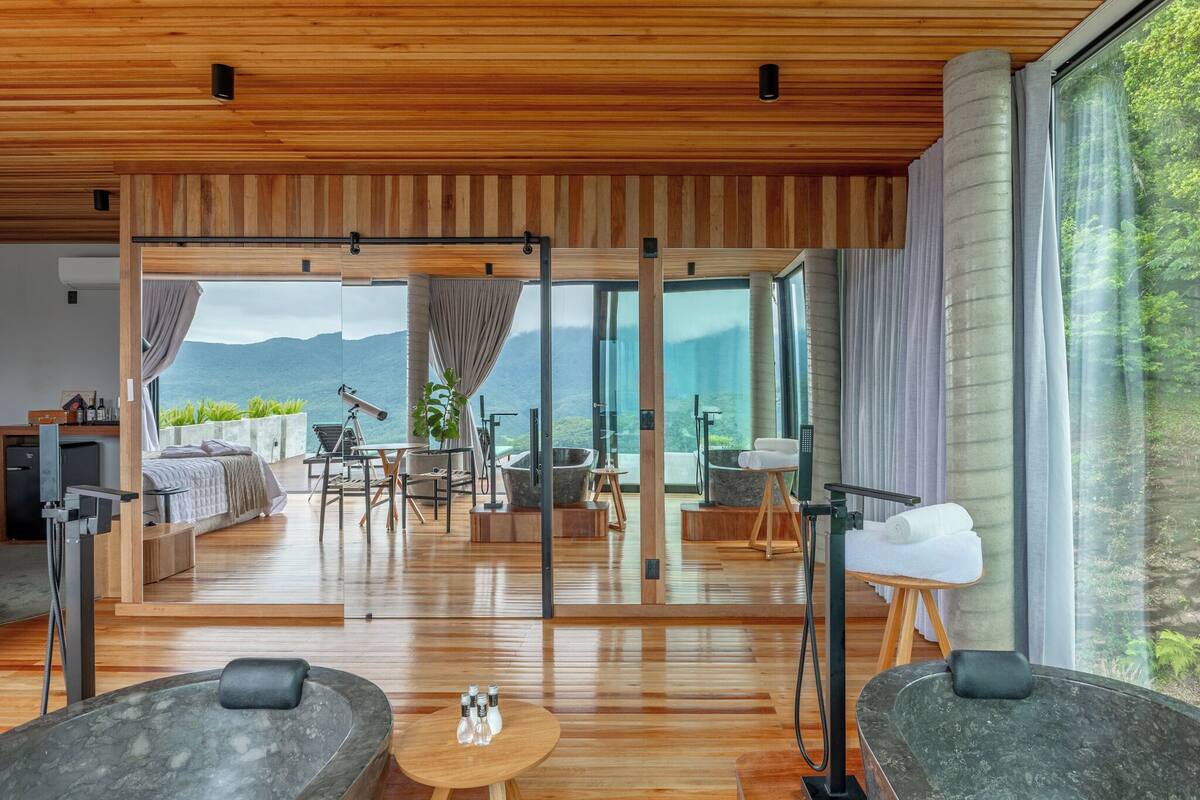 Ein modernes Hotelzimmer mit Holzboden, großen Fenstern, einem Bett, einer Sitzecke und einer Spa-Badewanne.