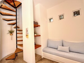 A spiral staircase with wooden steps and a plant, leading to a white wall with shelves and a light blue sofa.