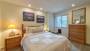 Quarto com cama, mesas de cabeceira, cômoda, janela e duas imagens penduradas na parede.