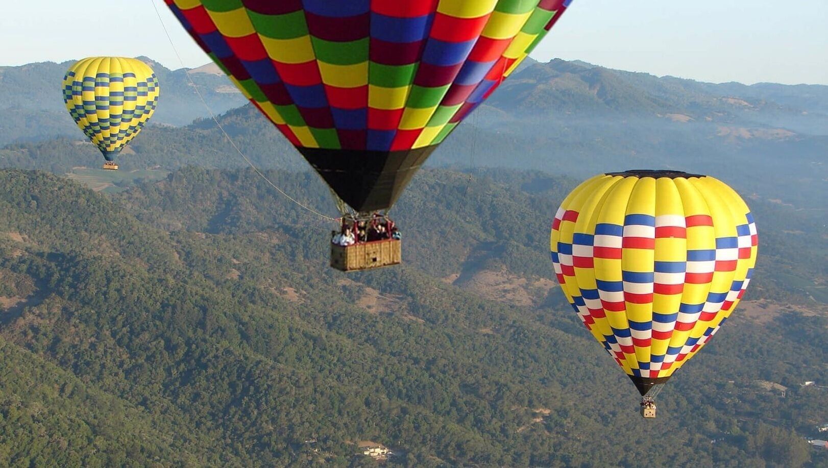 Drie luchtballonnen vliegen boven een bergachtig landschap.