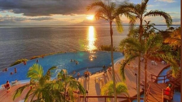 A resort pool area with a sunset view, wooden deck, and palm trees.