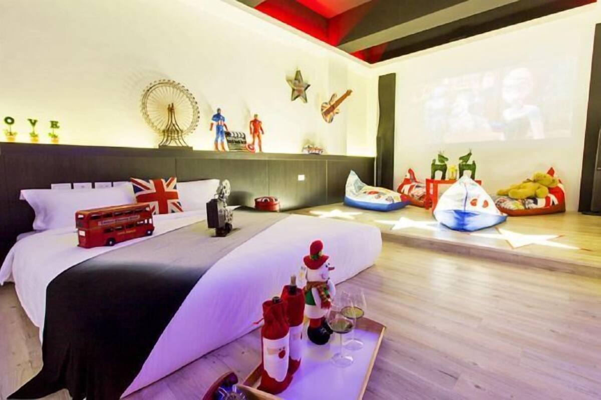 A hotel room with a bed, a projector screen, and various decorations including a Ferris wheel, figures, and a Christmas tree.