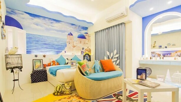 Una stanza con un letto, un divano in vimini, un tavolino, un affresco sulla parete e un tappetino d'ingresso.
