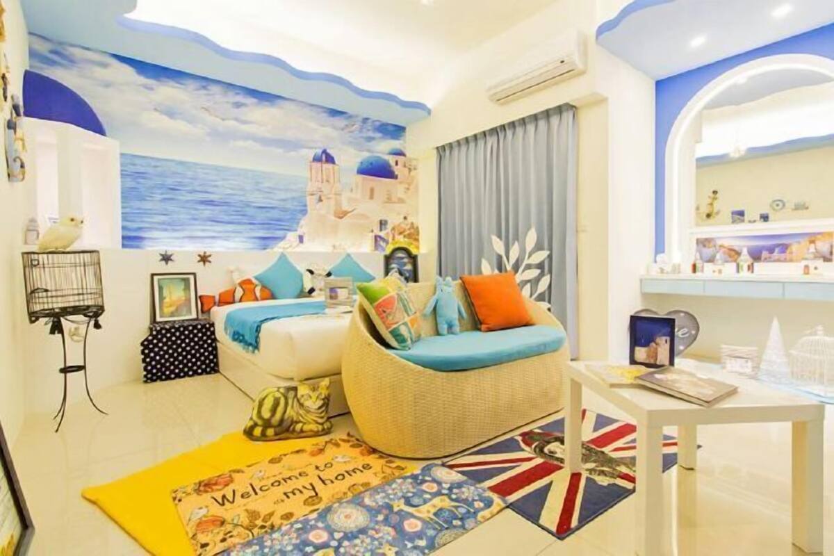 A room with a bed, a wicker sofa, a small table, a wall mural, and a welcome mat.