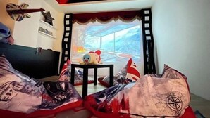 Una stanza con una grande finestra, un letto con copripiumino a motivi rossi e bianchi, un tavolino con un giocattolo e una parete con una bandiera Union Jack e una decorazione a stella.