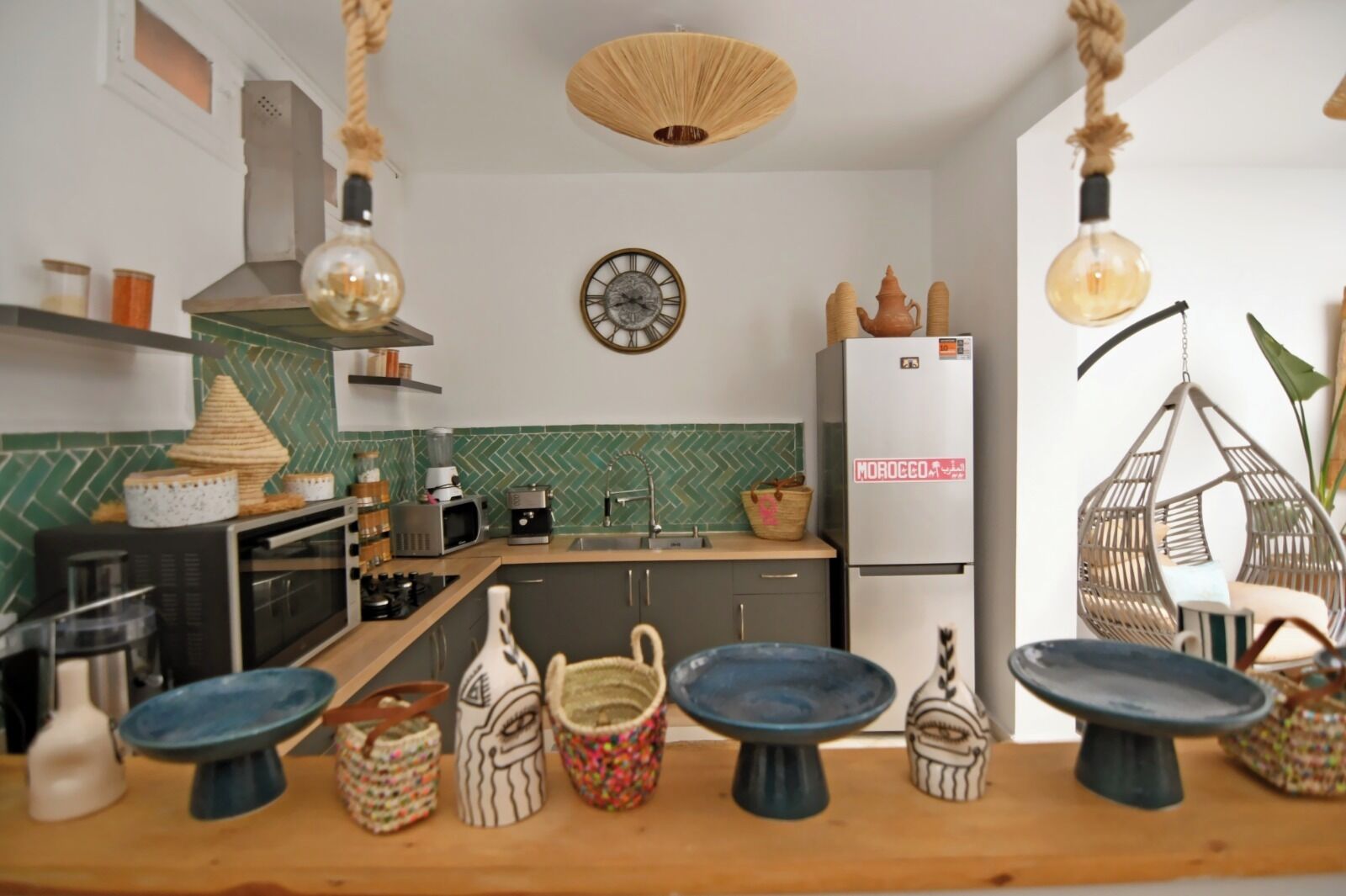 Una cocina moderna con un salpicadero verde en patrón de espiga, un refrigerador blanco y una lámpara colgante.