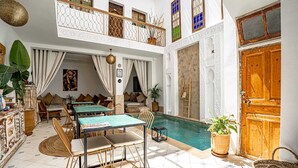 A spacious indoor pool area with a dining setup, a staircase, and a wooden door. - Riad Larbi Khalis (Marrakech)