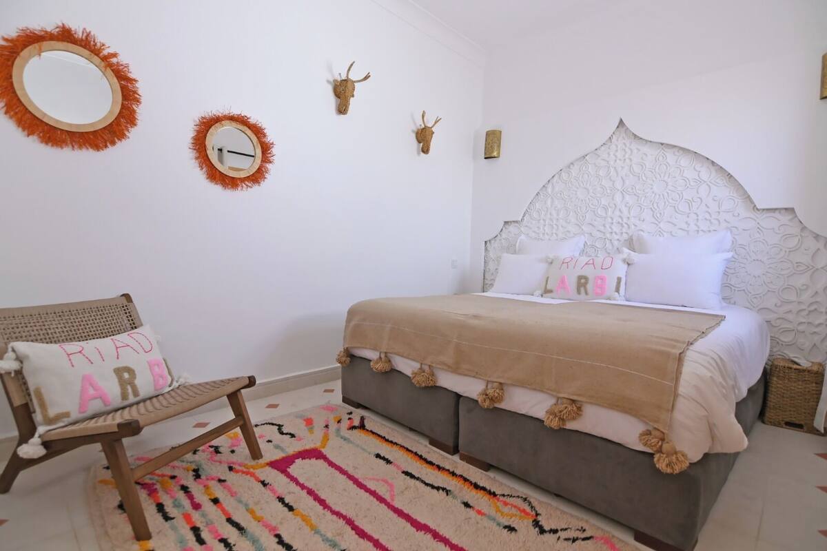 A bedroom with a bed, a chair, a rug, and wall decorations including a mirror and animal horns.