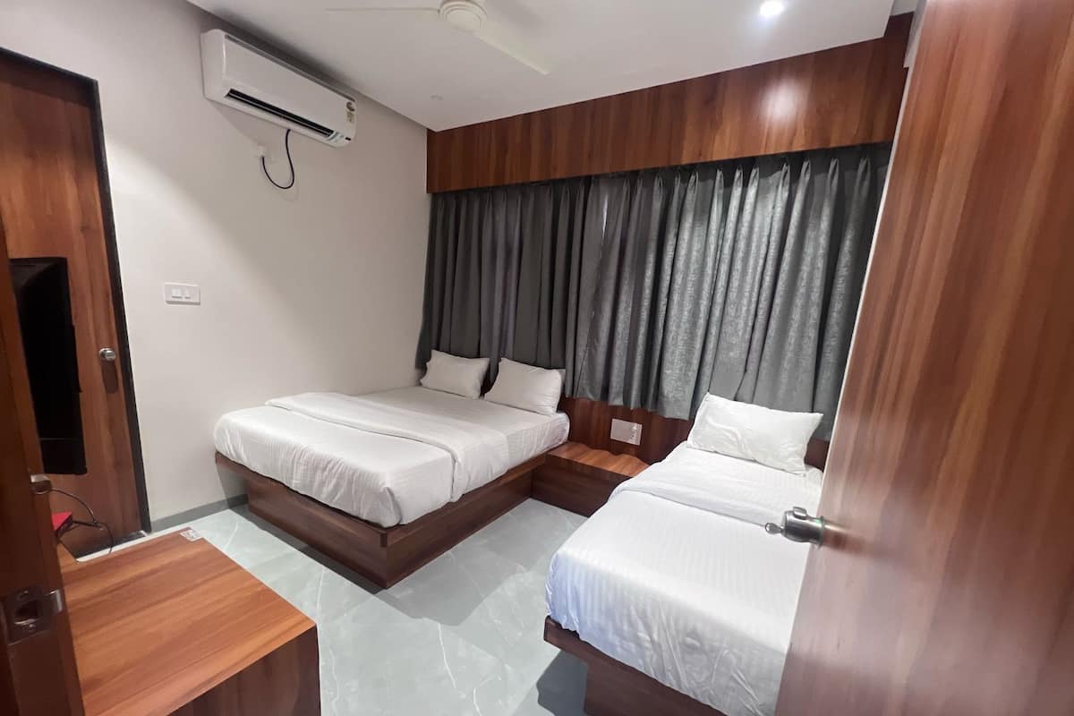 Habitació d'hotel amb dos llits, un escriptori de fusta, aire condicionat i ventilador de sostre.