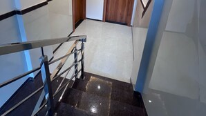 A modern staircase with glass railings and a polished black floor, leading to a hallway with wooden doors and recessed lighting. - HOTEL RUDRAKSH (Rahata)
