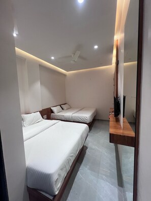 Une chambre avec deux lits, un ventilateur de plafond et une étagère en bois avec un miroir.