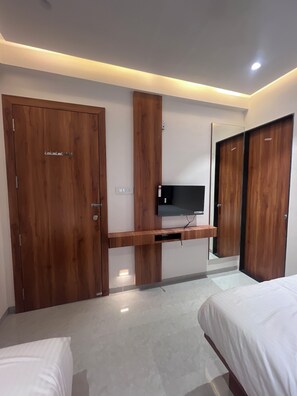 Een moderne slaapkamer met houten kasten, een flatscreen televisie bevestigd aan een houten plank, en een bed met witte beddengoed.