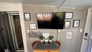 A dining area with a wooden table and chairs, a TV mounted on the wall, and framed pictures.
