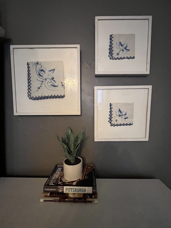 Un mur orné de trois motifs floraux bleus encadrés, et une petite plante en pot posée sur une pile de livres.