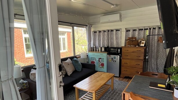 A compact living space with a kitchenette, a dining area with a table and chairs, and a sofa in the background.