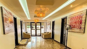 A hallway with a patterned wooden floor, two sofas, a standing lamp, and a door leading to an outdoor area. - Trisan Resident Hotel (Nairobi)