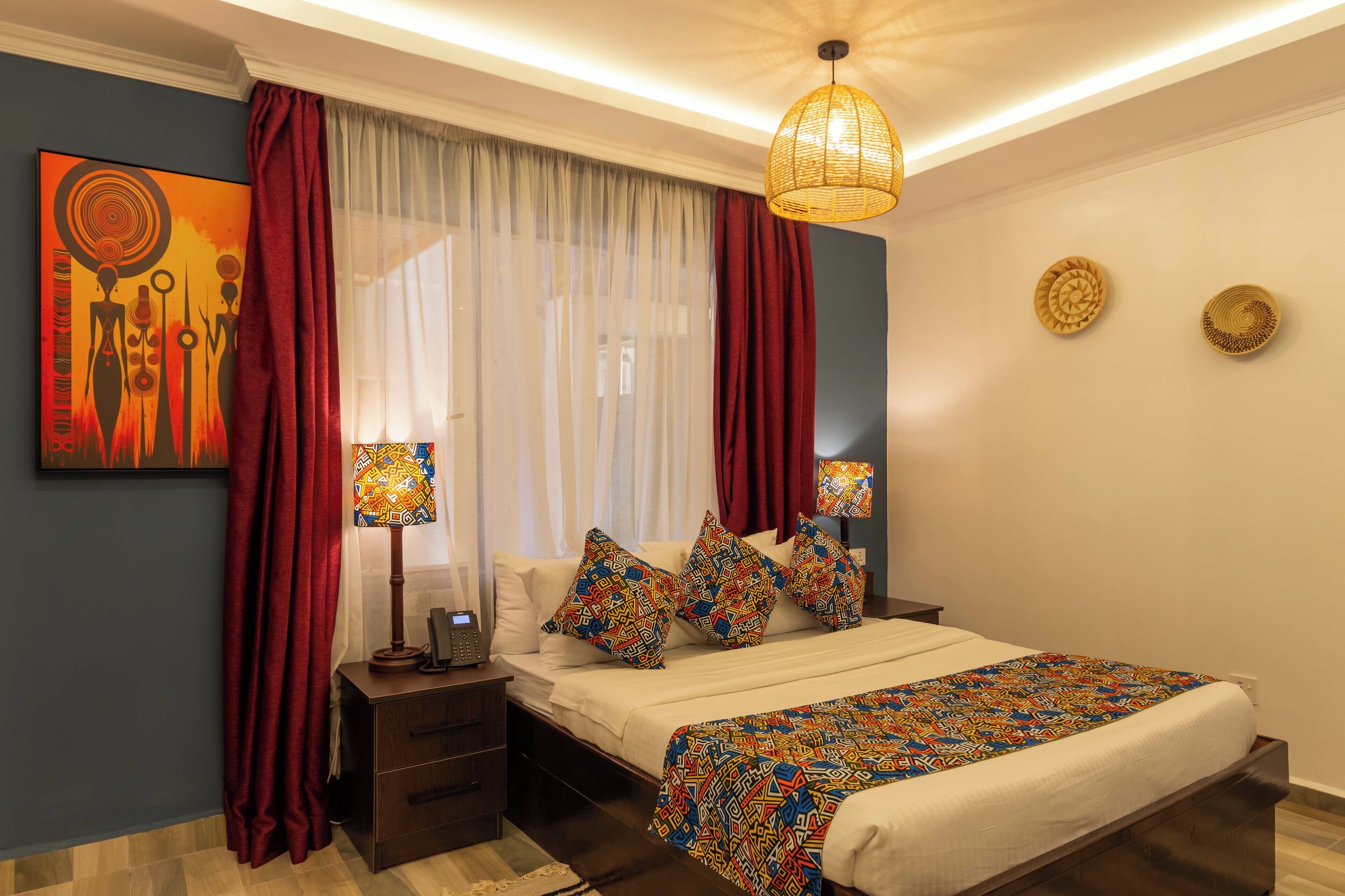 A bedroom with a bed, two bedside tables, a lamp, a window with curtains, and a wall art piece.