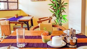 A dining area with a wooden table set for two, featuring a clear glass, a small potted plant, and a teapot. - Trisan Resident Hotel (Nairobi)