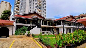 A multi-story building with a red-tiled roof, a covered outdoor area with potted plants, and a brick-paved parking area. - Trisan Resident Hotel (Nairobi)
