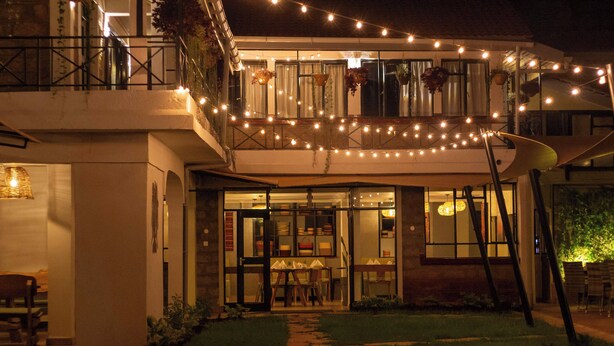 A two-story building with a glass entrance, outdoor seating, and string lights. - Trisan Resident Hotel (Nairobi)