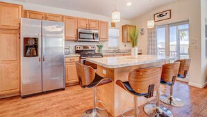 A modern kitchen with wooden cabinets, stainless steel appliances, and a central island with bar stools. - 2 bedroom 2 Bath Home w/Pool and beach access! (Jensen Beach)