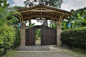 A wooden gate with a bamboo roof structure, surrounded by lush greenery.